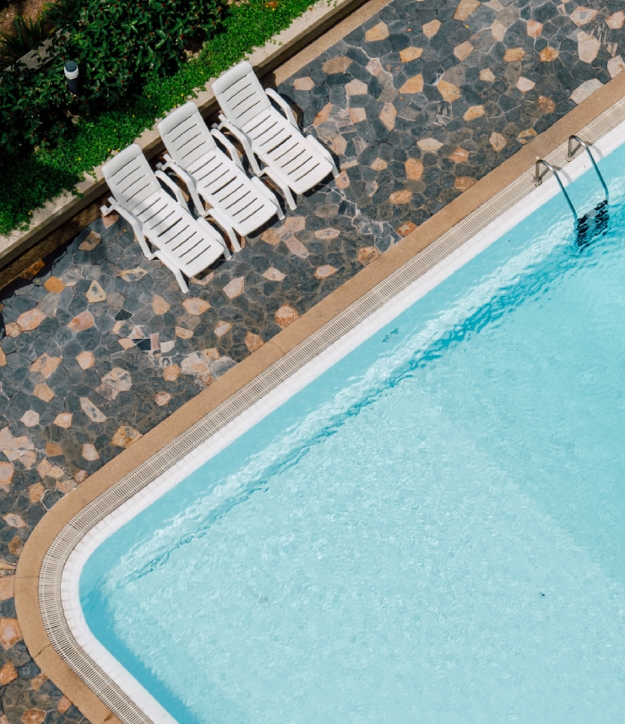 Piscine extérieure vue du dessus avec terrasse en pierre et trois transats blancs.