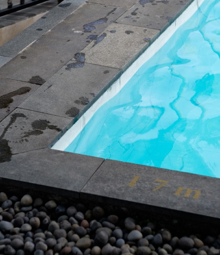 Bord de piscine avec margelles grises et galets décoratifs.
