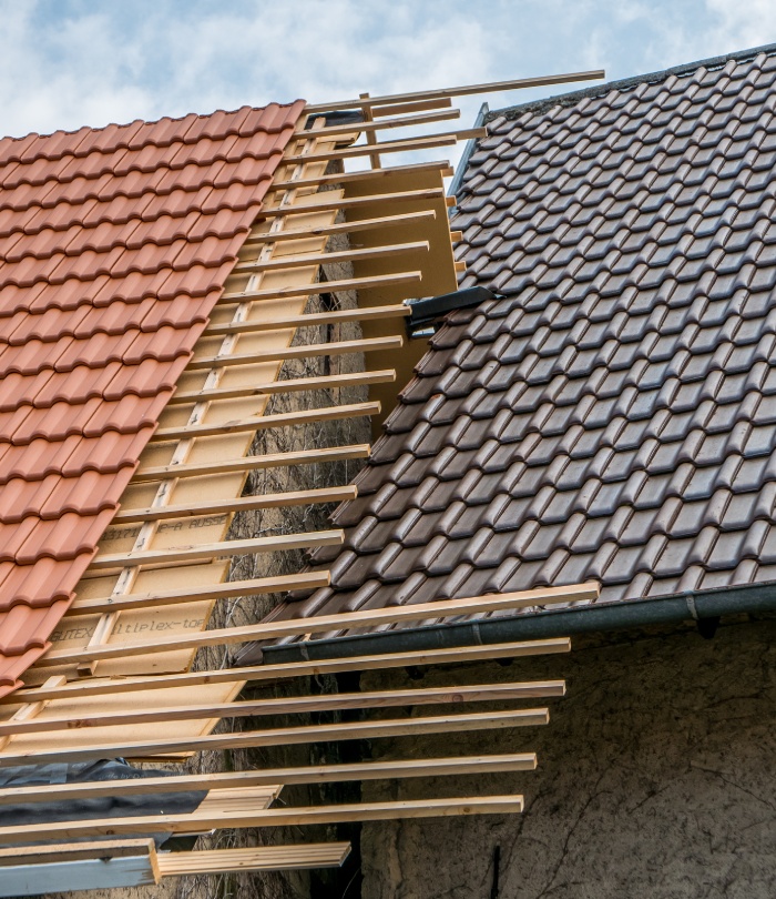 Toiture en cours de rénovation avec liteaux apparents entre des tuiles rouges et grises.